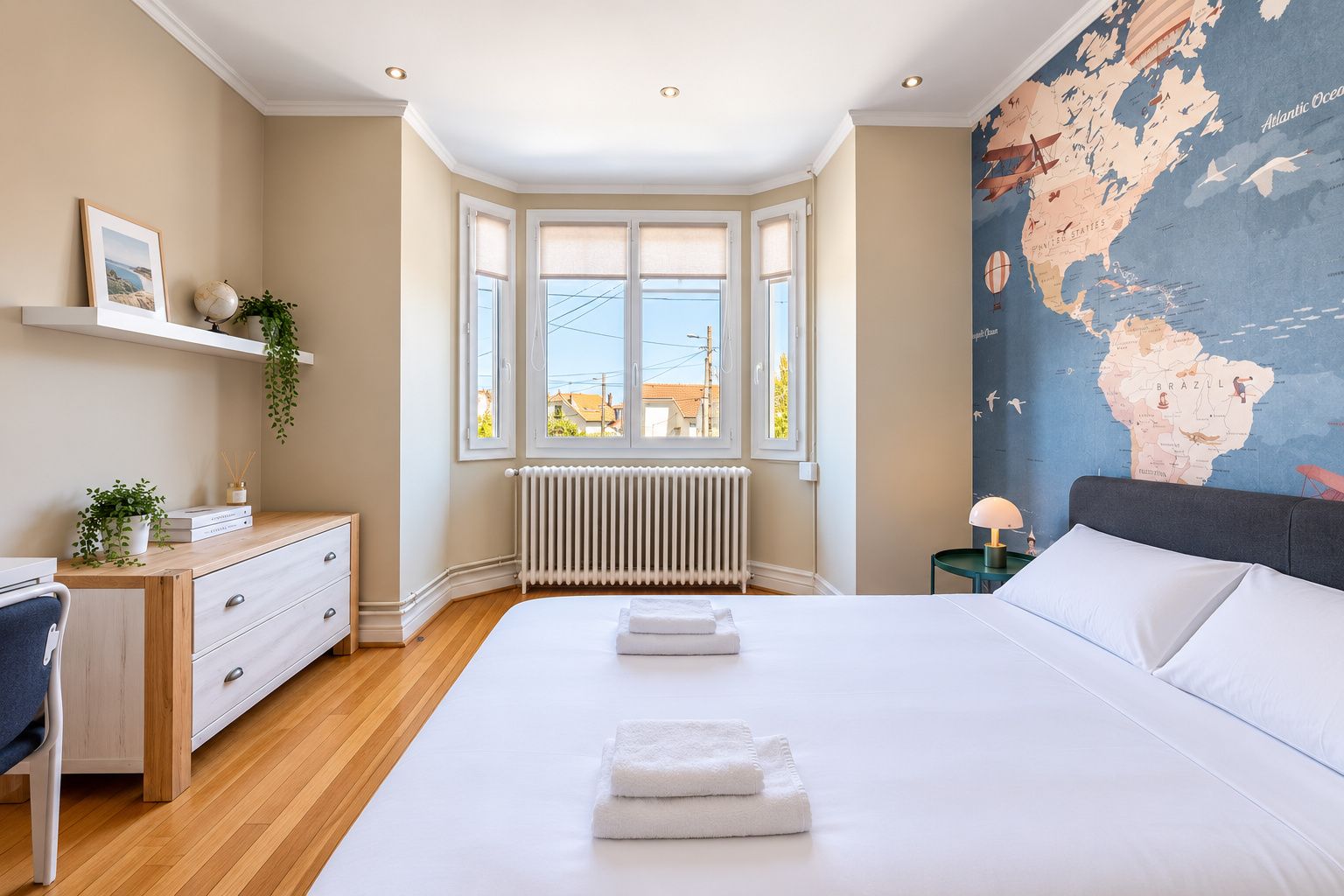 Un dormitorio con una cama grande, un escritorio con cajones, un radiador, un globo terráqueo y un mapa mundial en la pared.