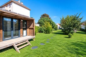 Een modern huis met een houten terras, grote ramen en een verzorgd gazon met staptegels.