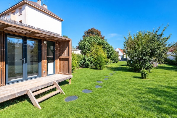 Een modern huis met een houten terras, grote ramen en een verzorgd gazon met staptegels.