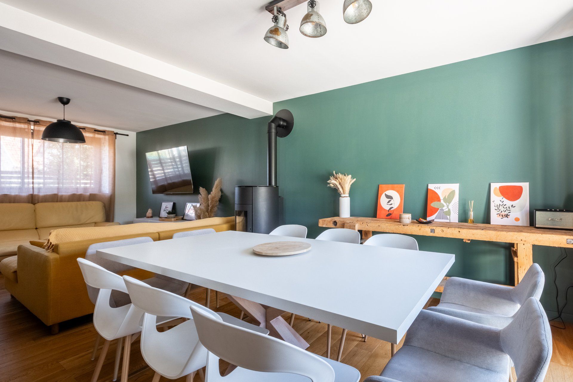 Un salon moderne avec une table à manger blanche, des chaises grises, un canapé et un téléviseur fixé au mur.