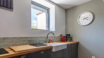 Une cuisine avec une fenêtre, un évier, une horloge et une machine à café.