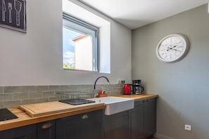Een keuken met een raam, een spoelbak, een klok en een koffiezetapparaat.