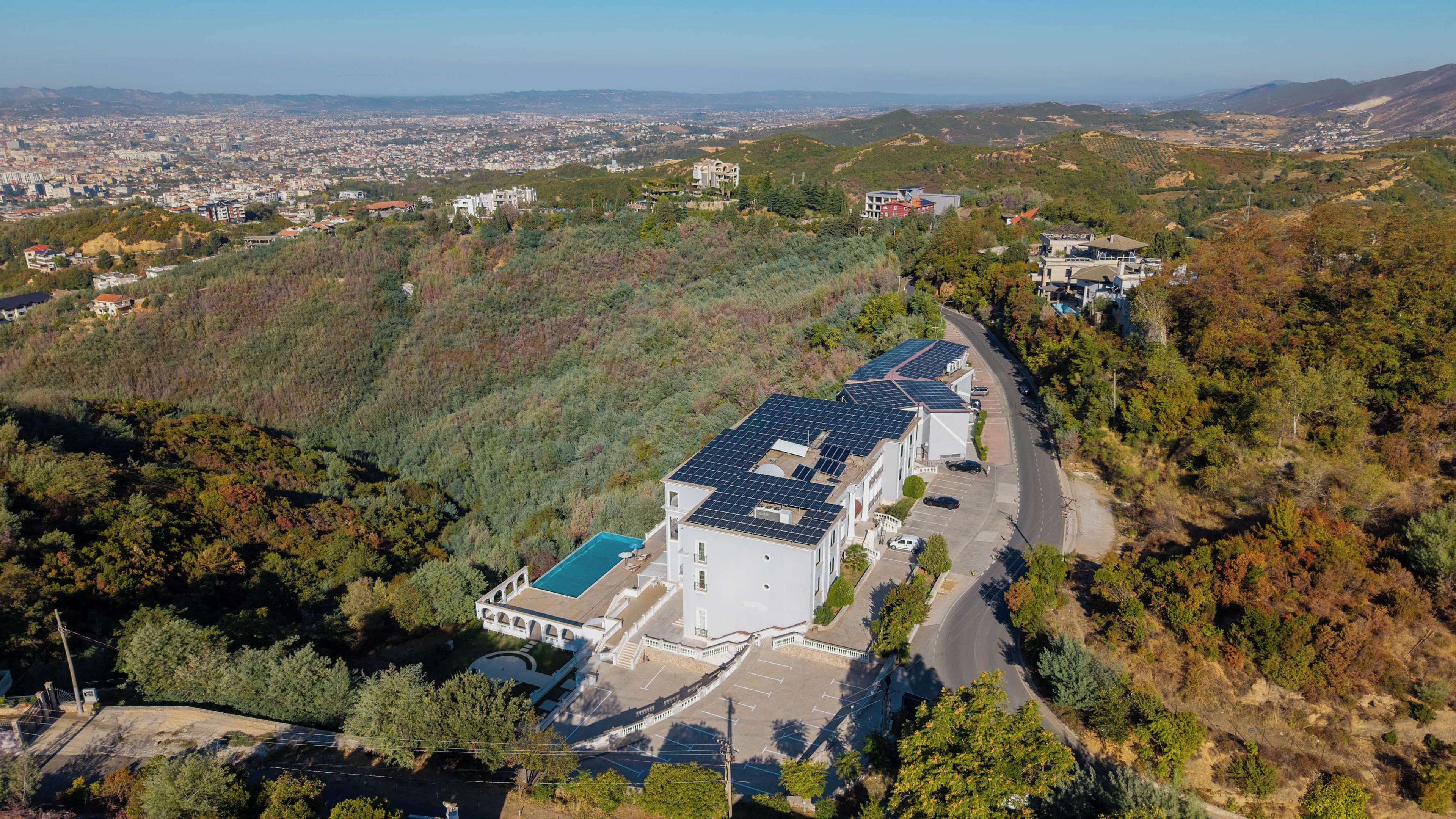 Zona residencial con una hilera de casas que tienen paneles solares en los techos, rodeada de terreno montañoso y vegetación.