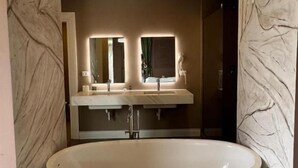 A modern bathroom with a freestanding bathtub, a double vanity with mirrors, and a marble wall design. - Jurgen Resort (Dajt)