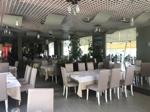 A restaurant interior with tables, chairs, ceiling fans, and potted plants.