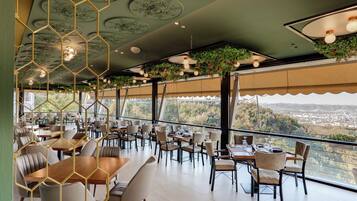 A restaurant with a terrace overlooking a cityscape, featuring hexagonal ceiling decorations and hanging plants.