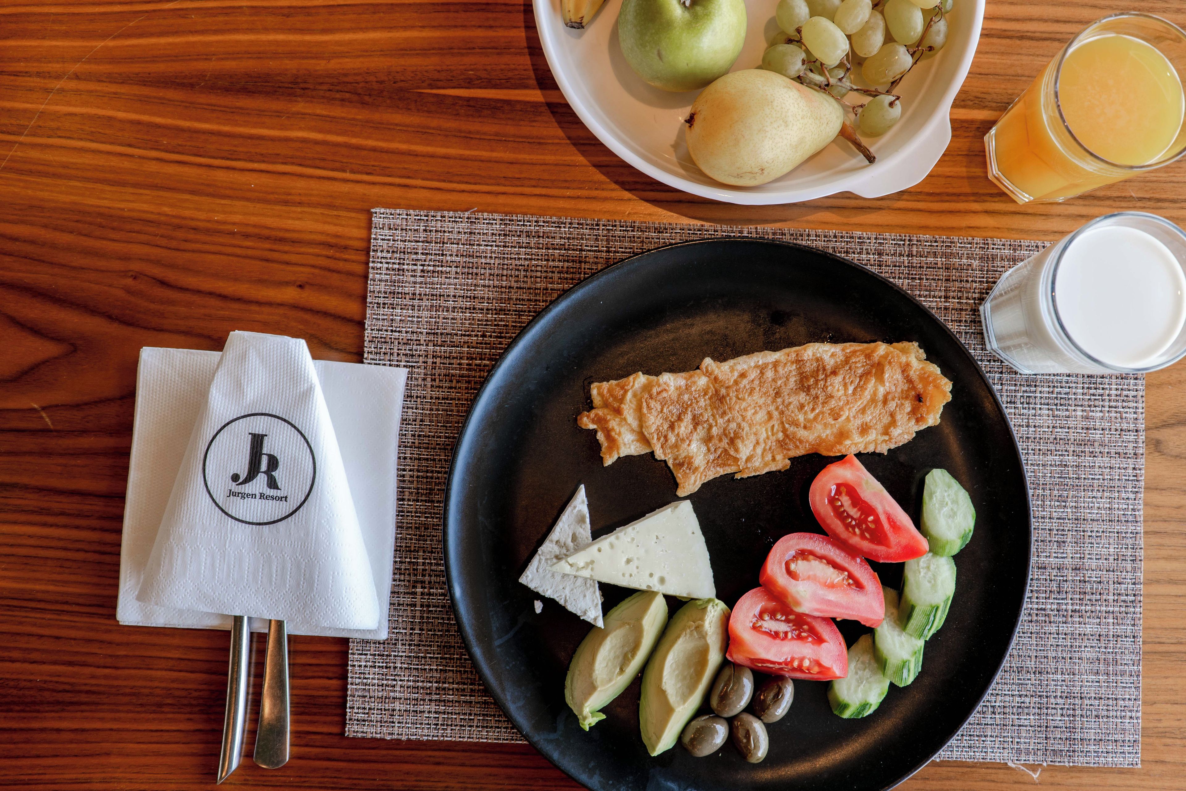 A breakfast plate with eggs, cheese, tomatoes, cucumbers, and olives on a black plate.