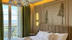 A hotel room with a large bed, a chandelier, a view through a glass door, and a wall with a tree design. - Jurgen Resort (Dajt)