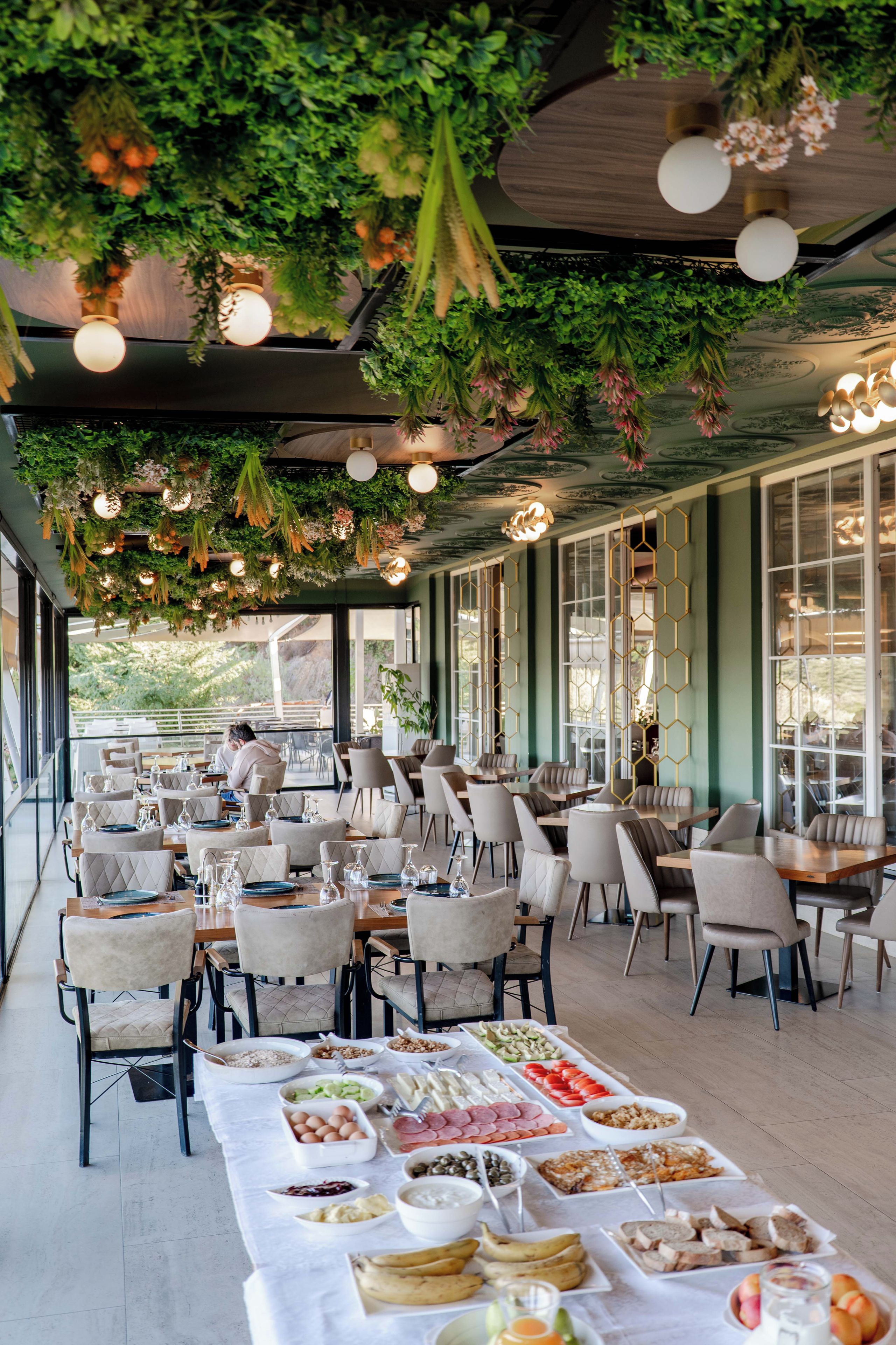 An outdoor dining area with tables set for a meal, surrounded by greenery and hanging lights.