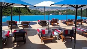 A rooftop lounge area with sun loungers and umbrellas, overlooking a cityscape and a body of water. - Jurgen Resort (Dajt)