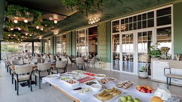 A dining area with tables set for a buffet, featuring a variety of food items and a beverage pitcher.