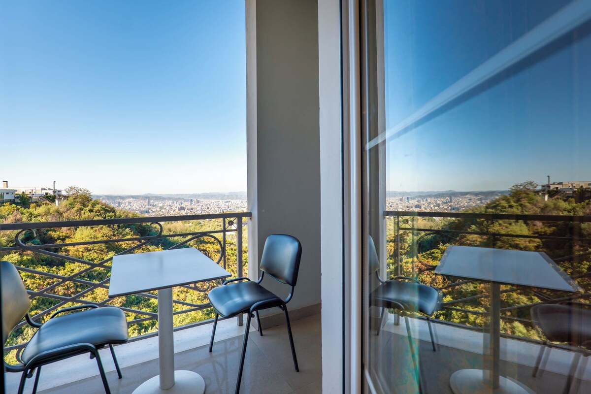 A balcony with two tables and chairs, offering a city view.