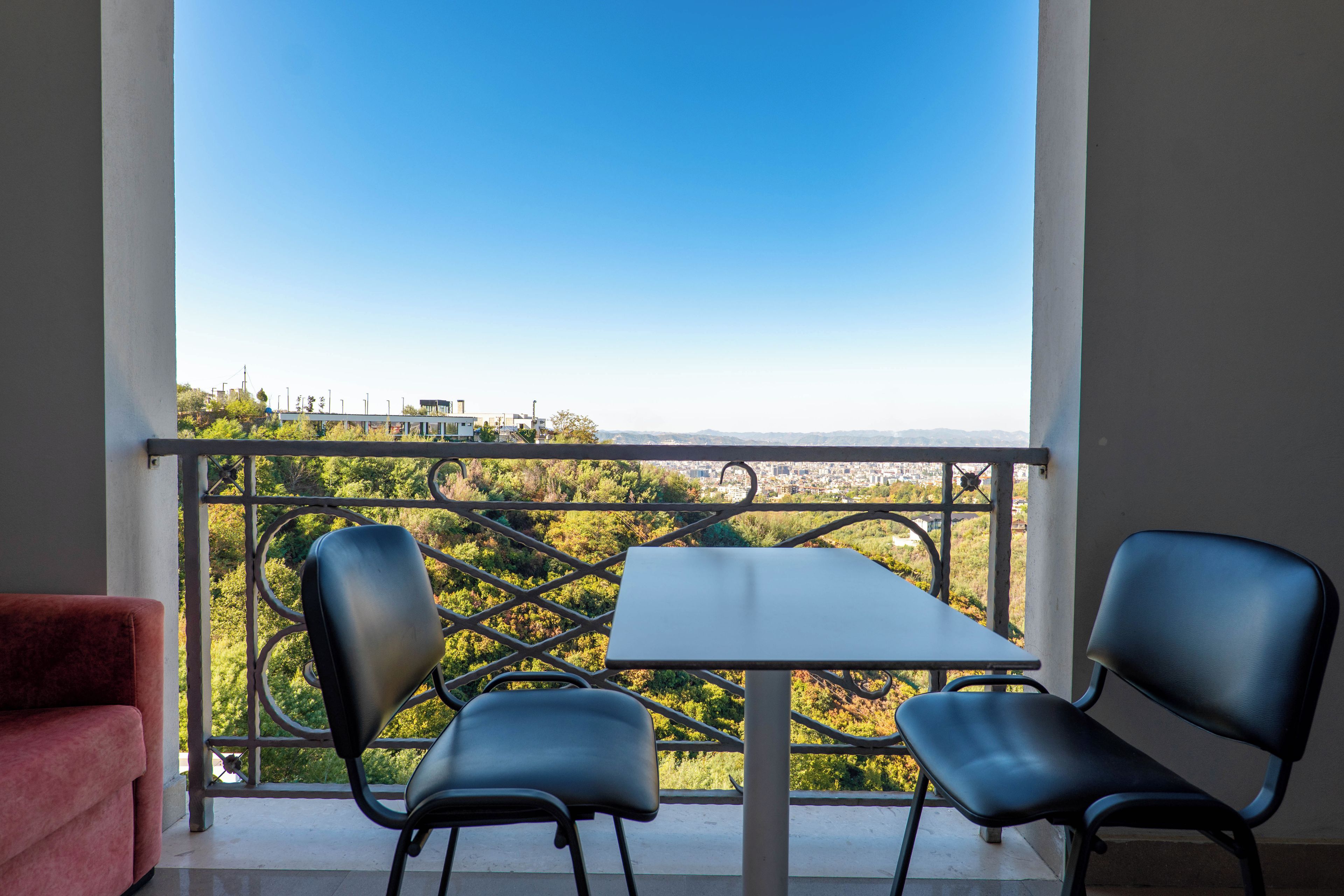 A balcony with a table and two chairs, overlooking a cityscape and greenery.