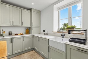A kitchen with light grey cabinets, a white countertop, a window with a view, and a black rack on the counter. - The Barn, an Exceptional Luxurious Retreat (Newburgh)