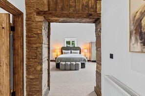 A bedroom with a stone archway, a bed with a grey duvet, two bedside lamps, and a radiator. - The Barn, an Exceptional Luxurious Retreat (Newburgh)