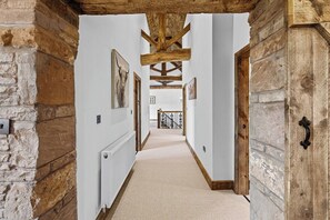 A hallway with exposed wooden beams, stone walls, and a carpeted floor. - The Barn, an Exceptional Luxurious Retreat (Newburgh)