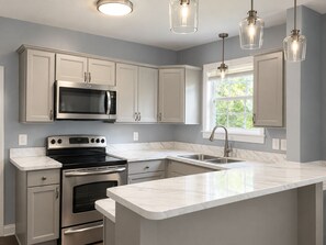 Una cocina moderna con armarios blancos, electrodomésticos de acero inoxidable, encimera de mármol e iluminación colgante.