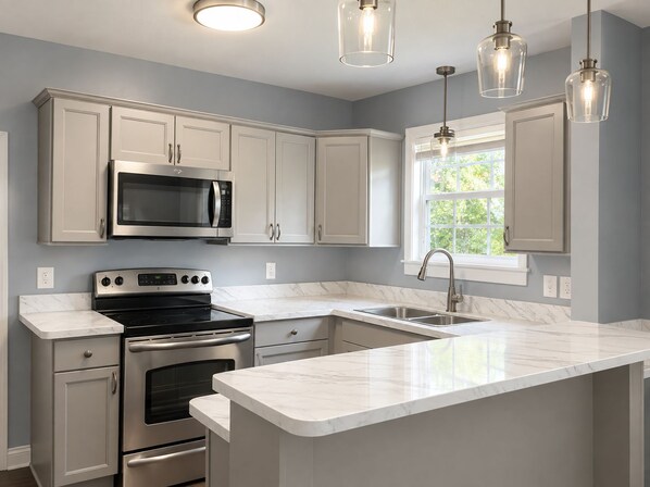 A modern kitchen with white cabinets, stainless steel appliances, a marble countertop, and pendant lighting.
