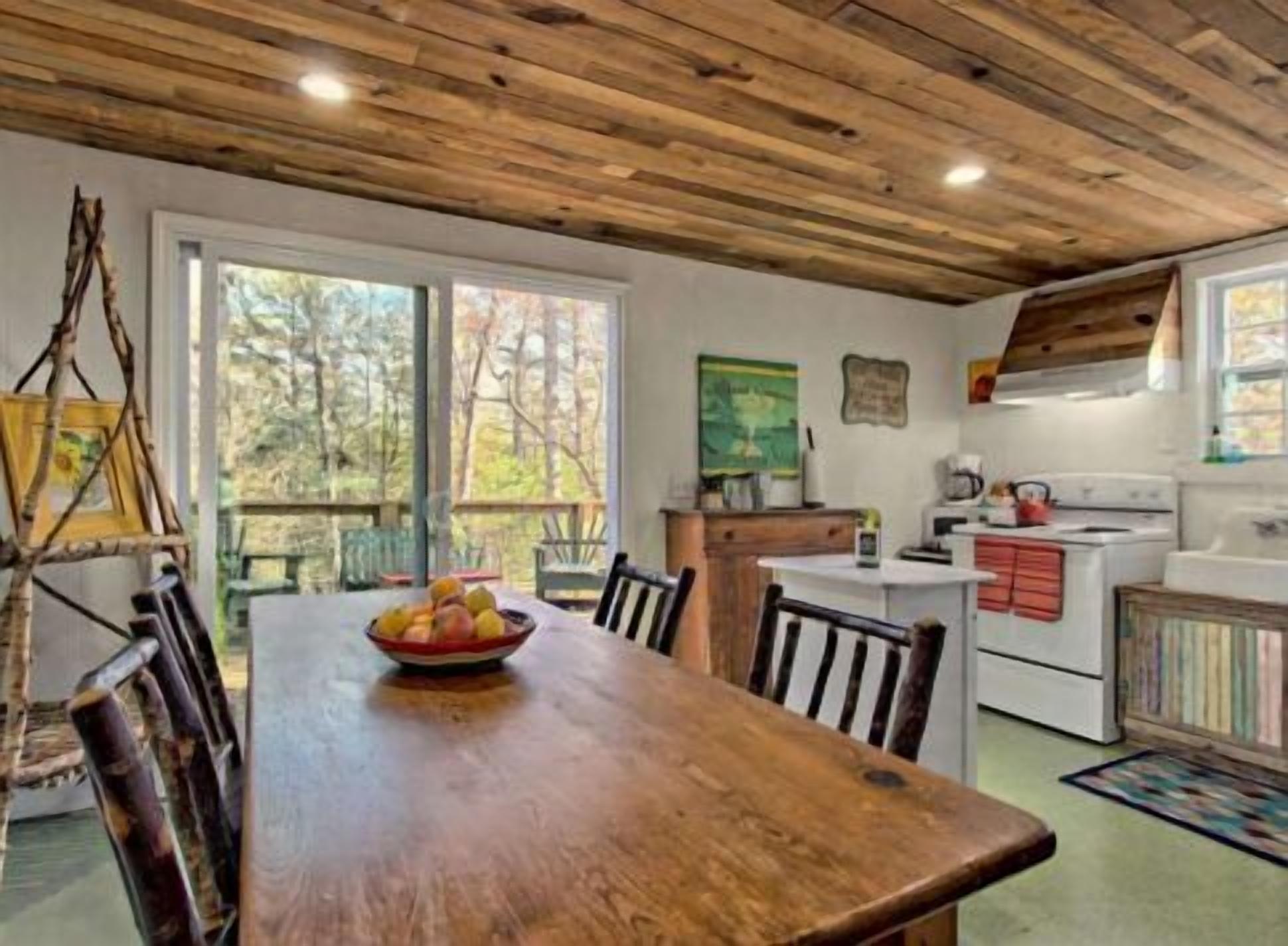 A wooden dining table with chairs, a kitchen area with a stove, and a painting on the wall.