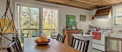 A wooden dining table with chairs, a kitchen area with a stove, and a painting on the wall.