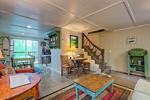 Un salon chaleureux avec une table basse en bois, un coin repas avec des chaises, un coin cuisine équipé d’un four à micro-ondes et un escalier au design rustique.