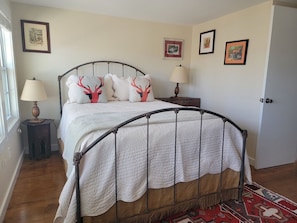 A bedroom with a metal-framed bed, white bedding, and decorative pillows. There are two bedside tables with lamps, a rug on the floor, and framed pictures on the walls.
