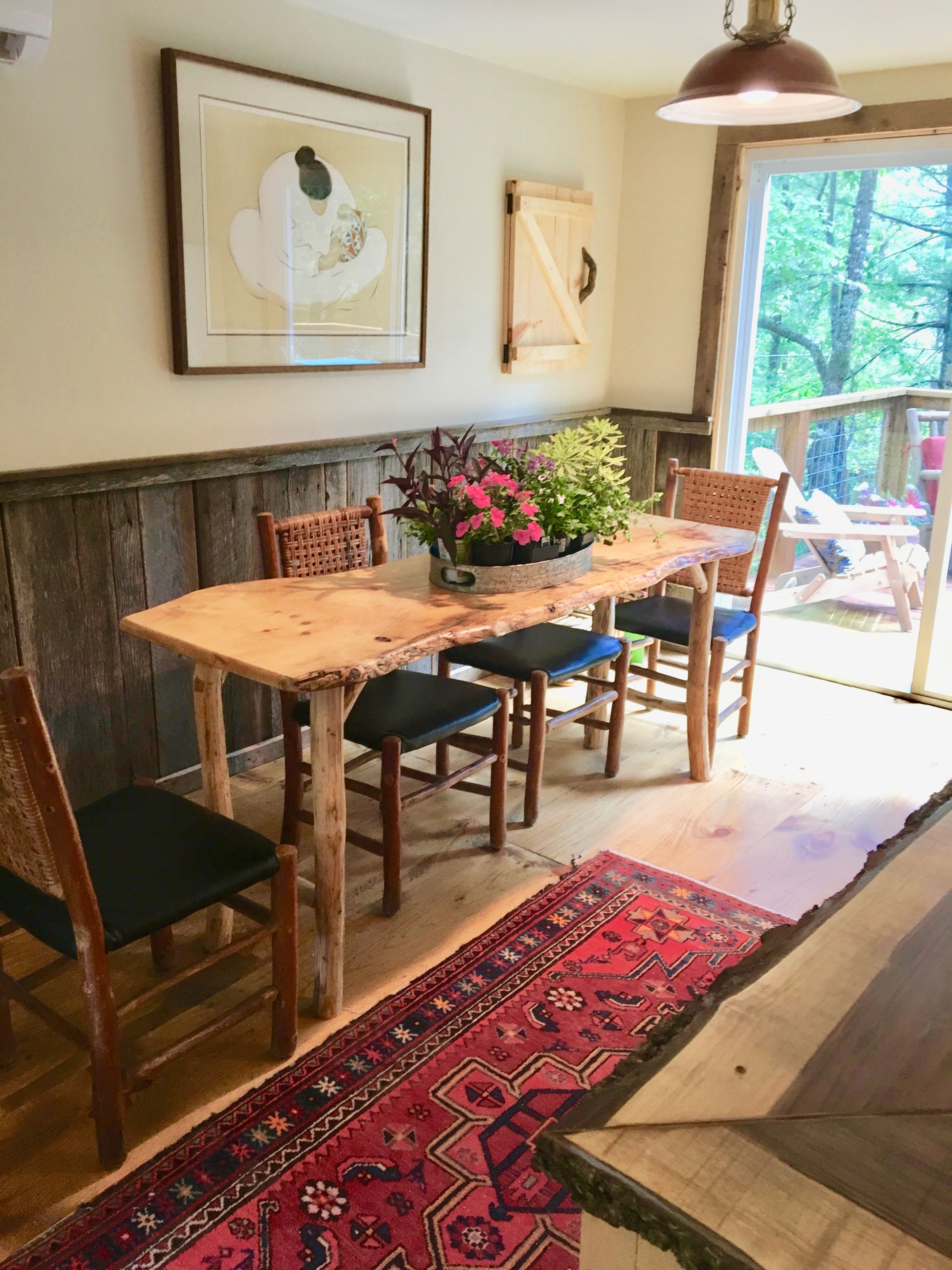 Una mesa de comedor de madera con sillas, un jarrón de flores y una alfombra estampada.