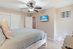 Une chambre à coucher avec un lit, un ventilateur de plafond, un téléviseur fixé au mur et une porte.