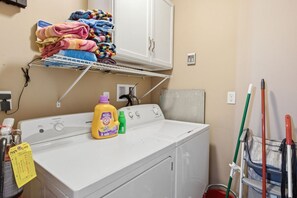 A laundry area with a washing machine, a shelf with folded towels, and cleaning supplies. - Coastal Dreams | Golf Cart | 11 Pools | Beach Access | Sleeps 7 (Panama City Beach)