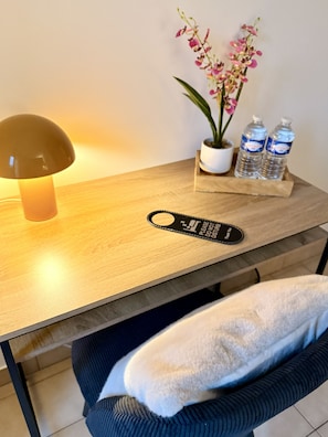 Una mesa de madera con una lámpara, una orquídea en maceta y dos botellas de agua.