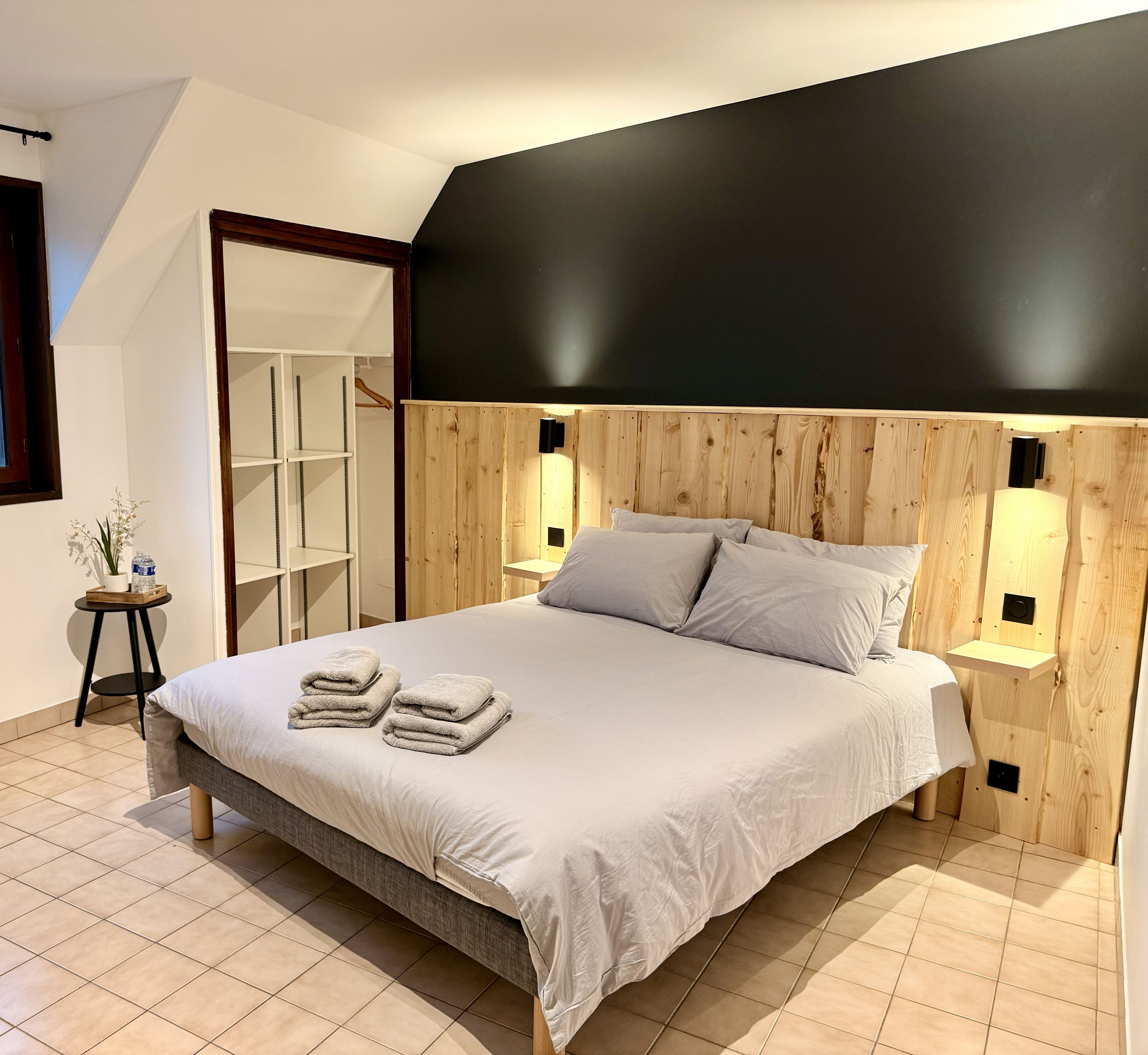 Un dormitorio moderno con cama, mesita de noche, cabecera de madera y estante empotrado.