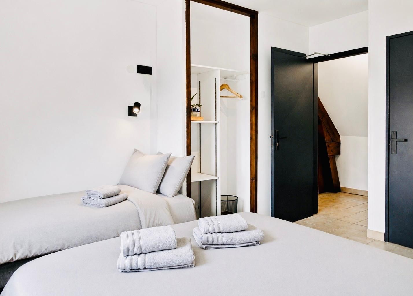 A modern hotel room with two beds, a wardrobe, and a staircase.