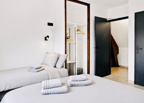 A modern hotel room with two beds, a wardrobe, and a staircase.