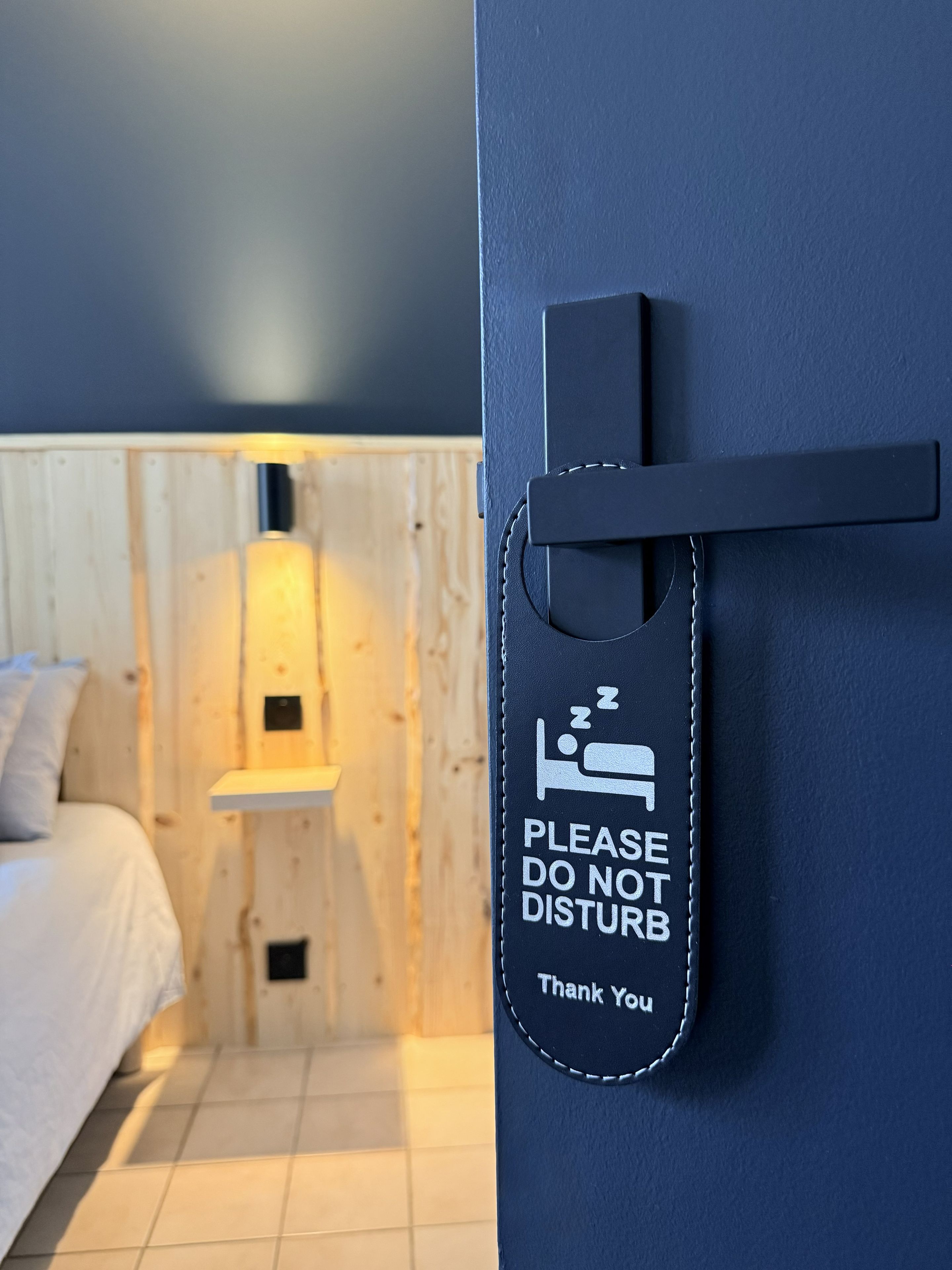 Une chambre d’hôtel avec un lit, une table de chevet et un panneau fixé au mur, orné d’une icône représentant un lit et d’un texte.