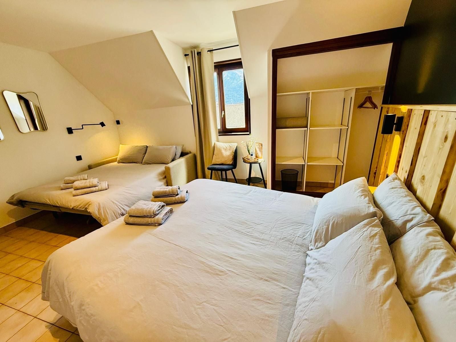 Ein Hotelzimmer mit zwei Betten, einem Fenster, einem Sessel und einem Kleiderschrank.