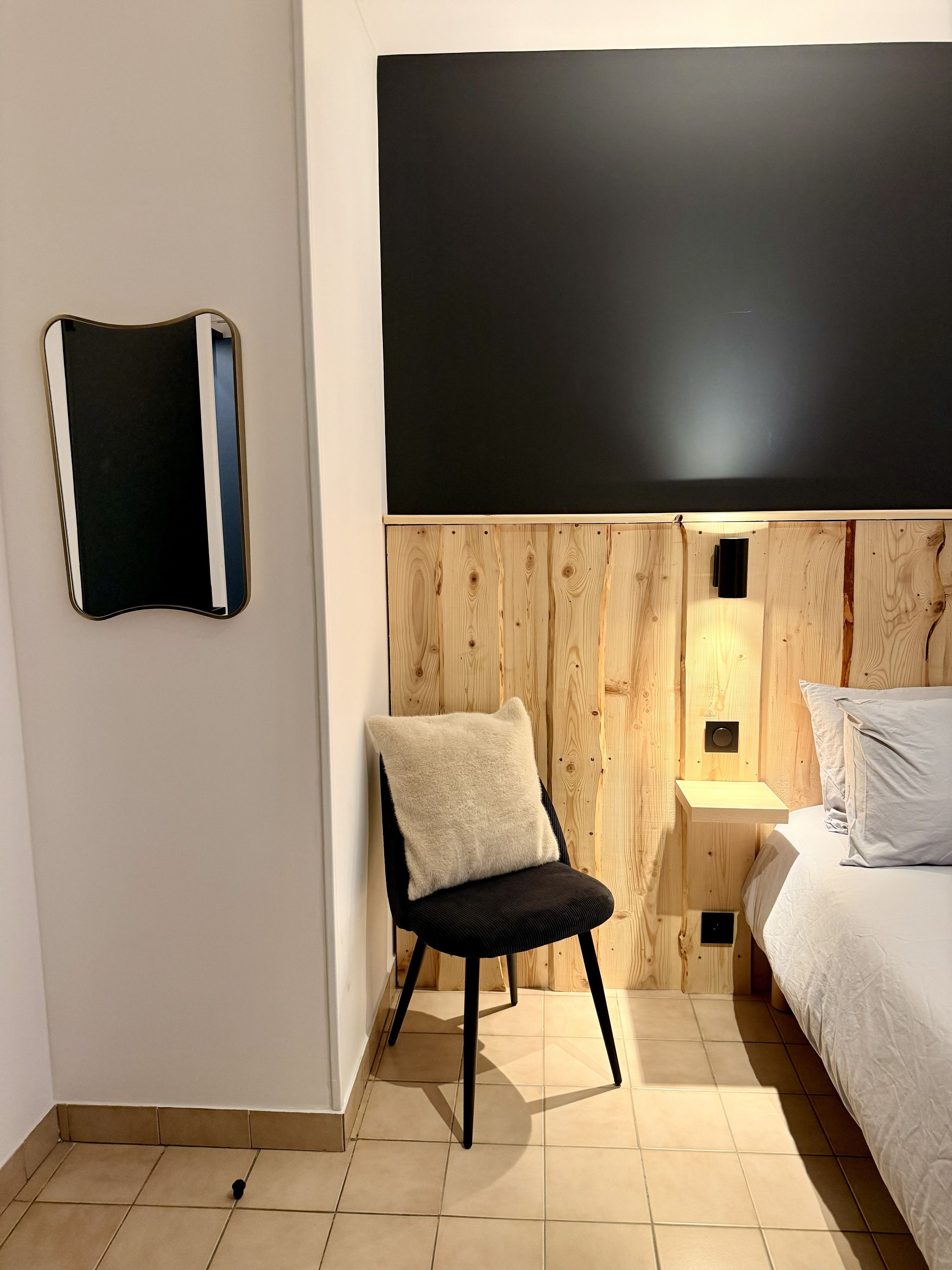 A bedroom with a bed, a chair, a bedside table, a wall-mounted TV, and a wooden panel wall.