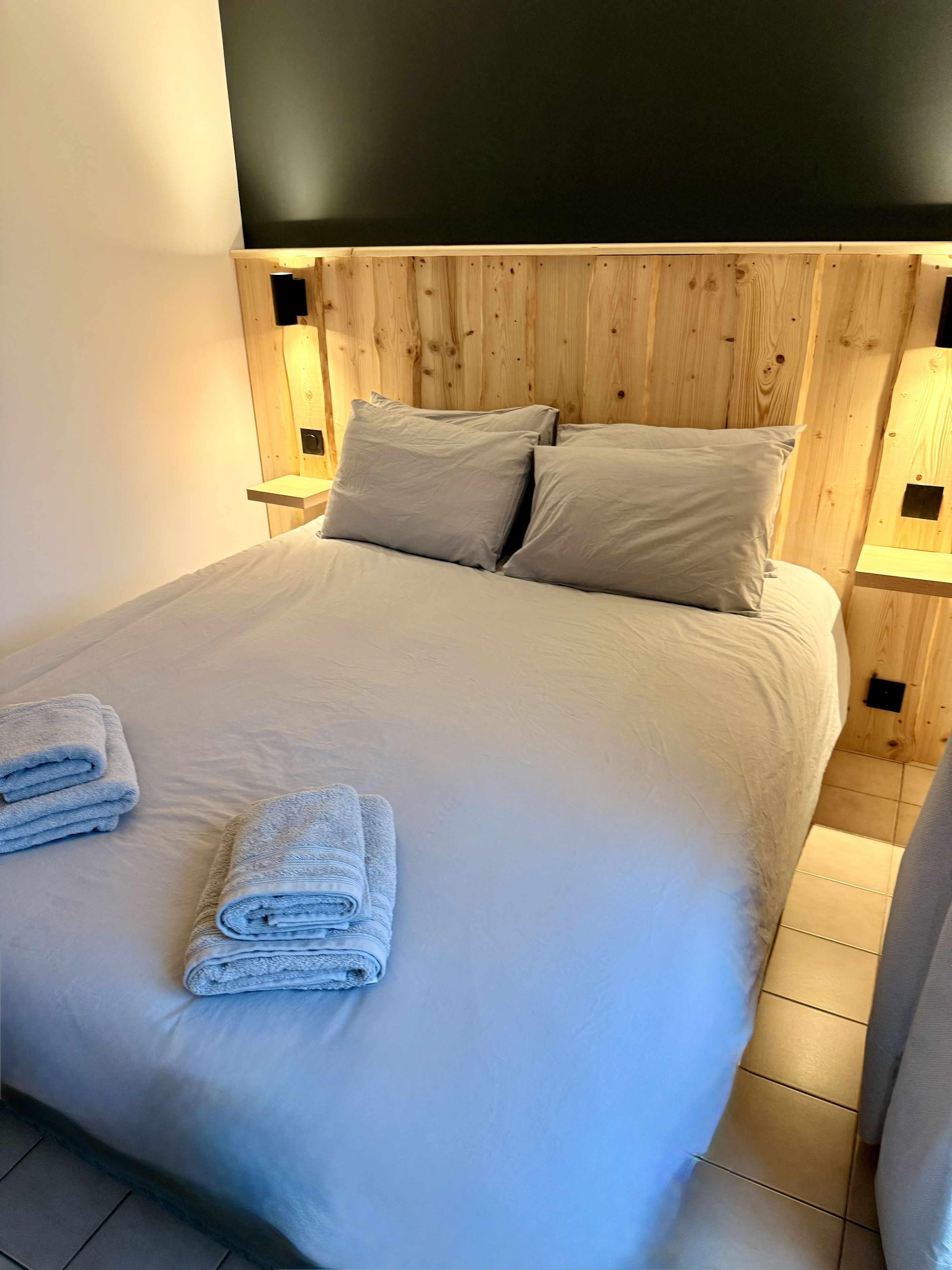 Una cama con cabecera de madera, dos almohadas y dos lámparas de noche.