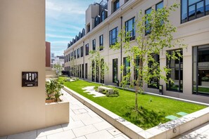 A modern building with a courtyard, a sign indicating 'HOUSTON,' and a well-maintained lawn with young trees. - Azure: 1BR with AC & Parking | Urban Garden (Porto)