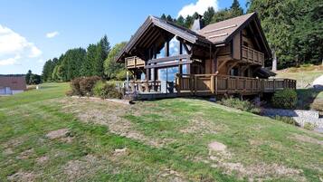 A wooden cabin with a balcony, surrounded by a grassy landscape and trees.
