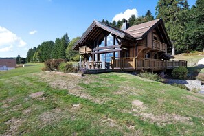 A wooden cabin with a balcony, surrounded by a grassy landscape and trees. - Chalet 'L'Alpage' with Mountain View, Sauna and Jacuzzi (Gérardmer)