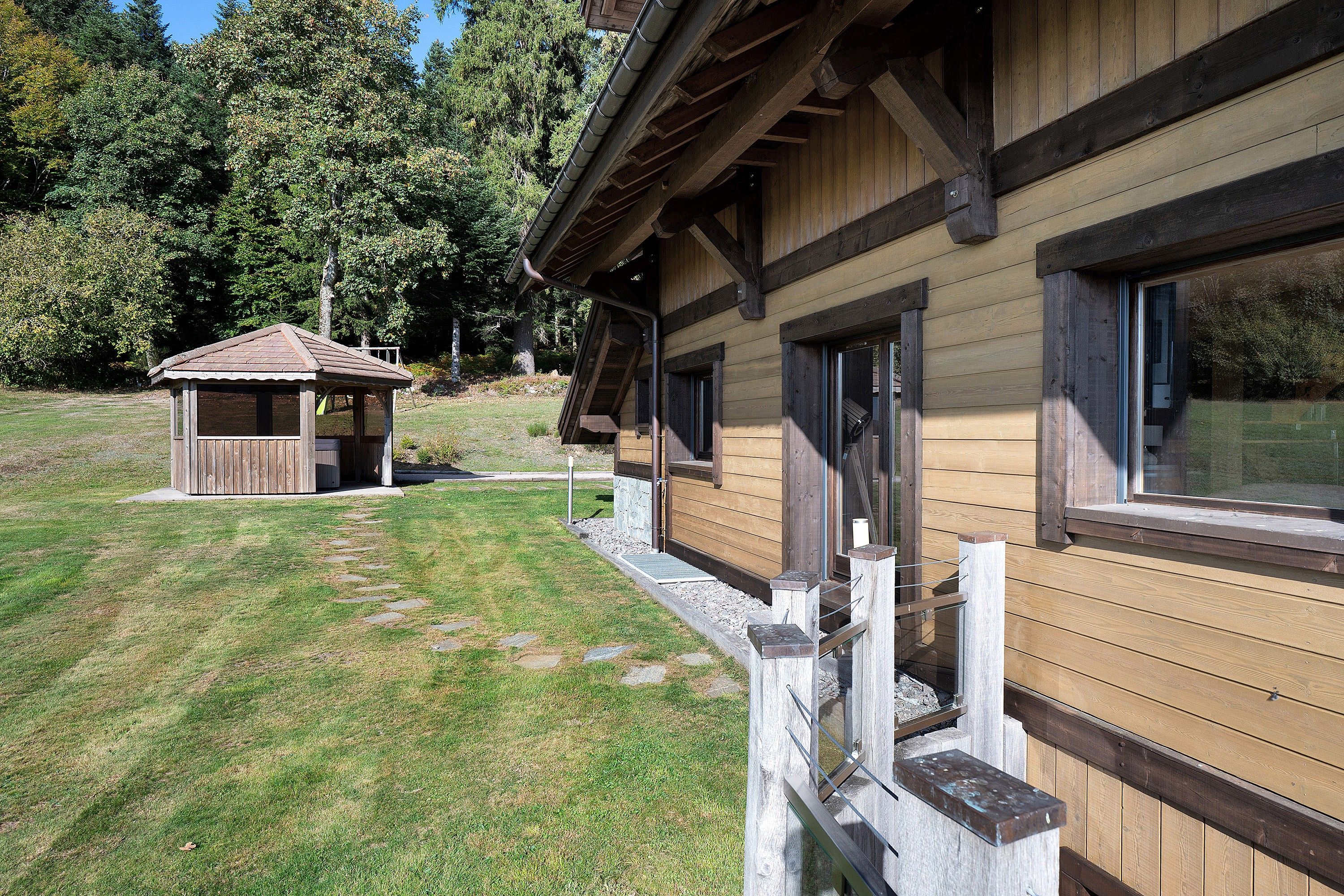 A wooden cabin with a covered porch and a small adjacent shed, surrounded by a grassy area and trees.