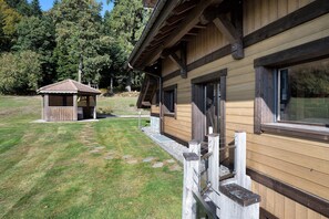 A wooden cabin with a covered porch and a small adjacent shed, surrounded by a grassy area and trees. - Chalet 'L'Alpage' with Mountain View, Sauna and Jacuzzi (Gérardmer)