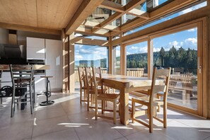 A spacious dining area with a large wooden table and chairs, a bicycle, and a kitchen area with modern appliances.
