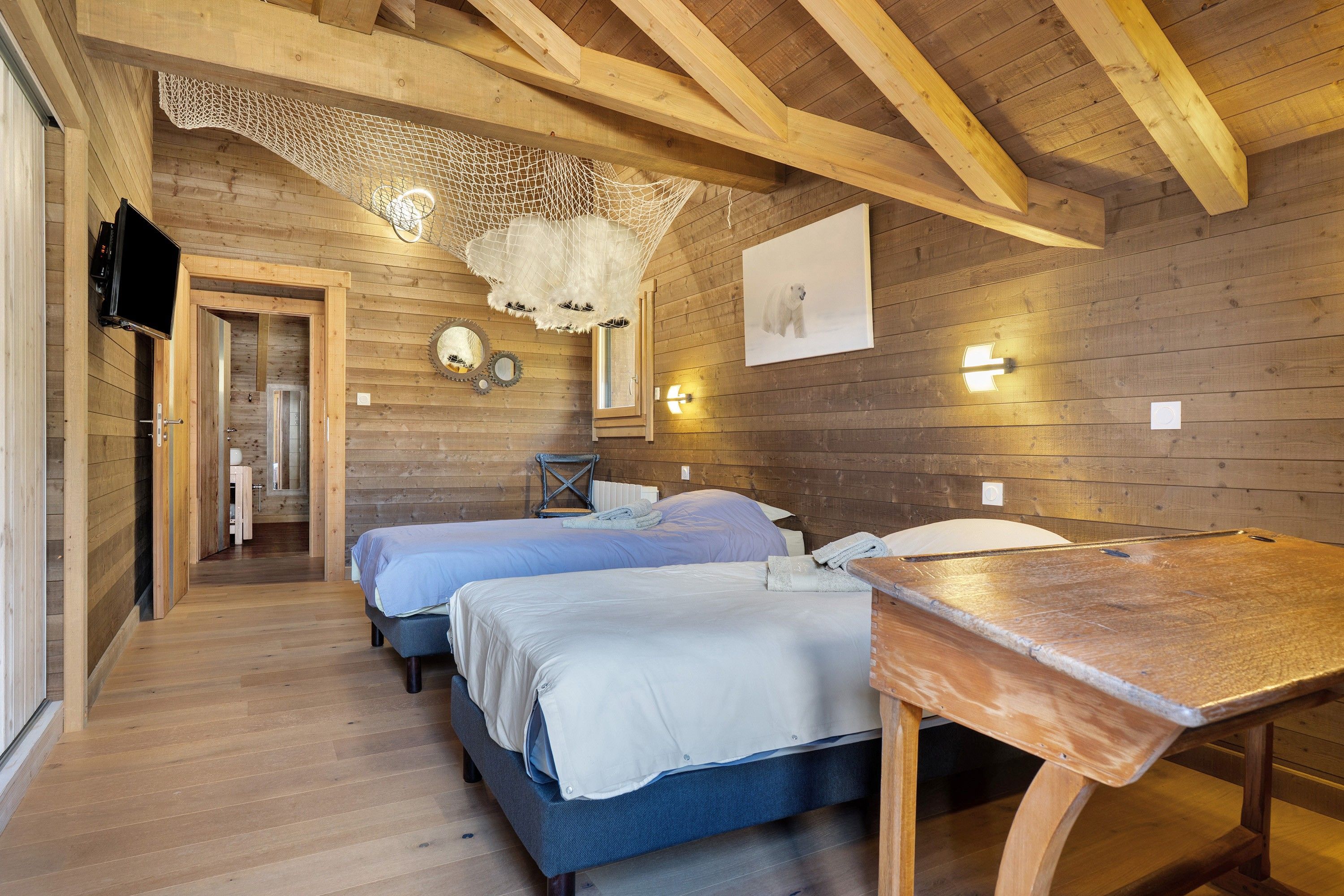 A wooden cabin room with two beds, a table, and a television.