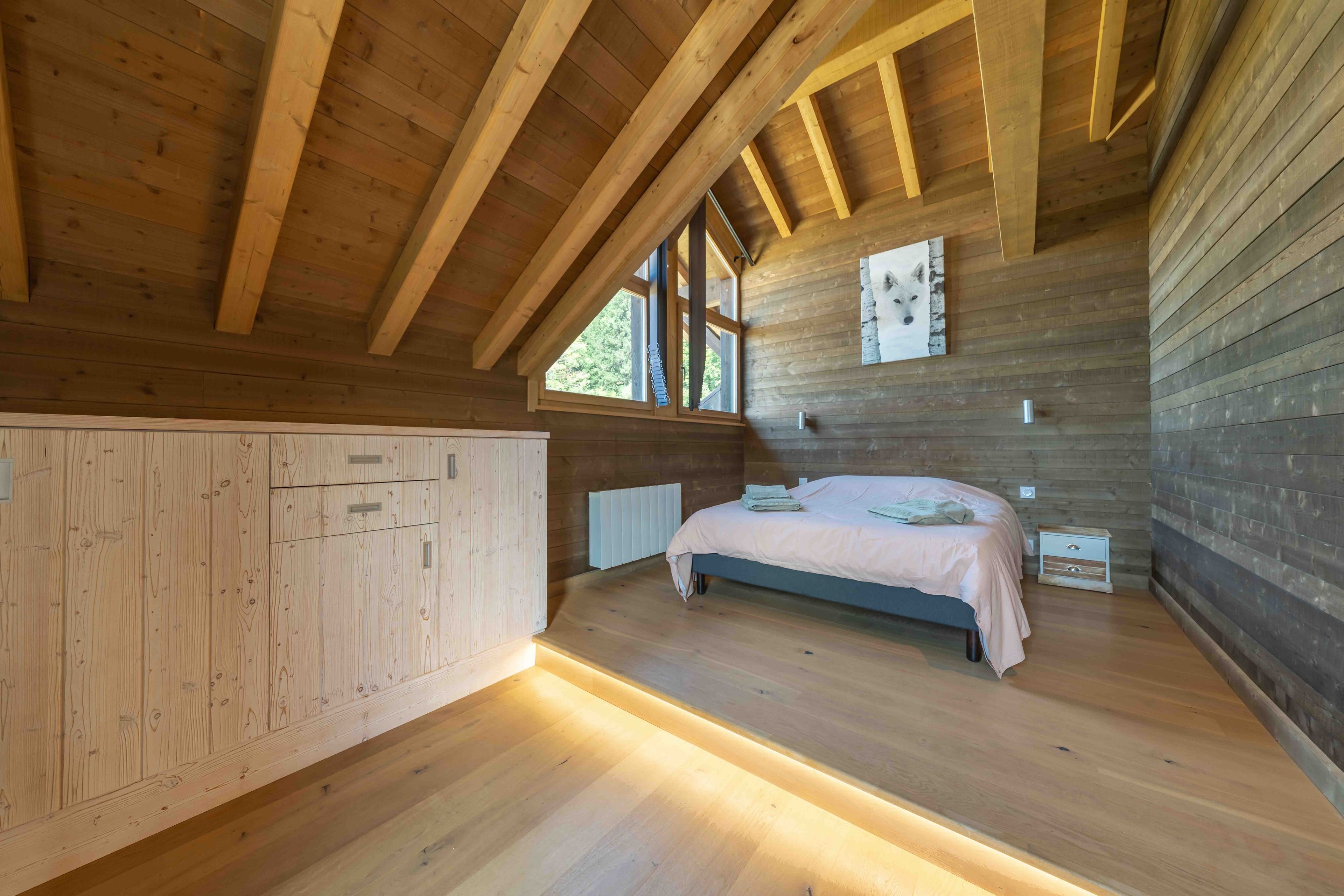A wooden interior with a bed, a radiator, and a window.