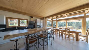 A modern kitchen with a wooden ceiling, large windows, and a dining area with bar stools.