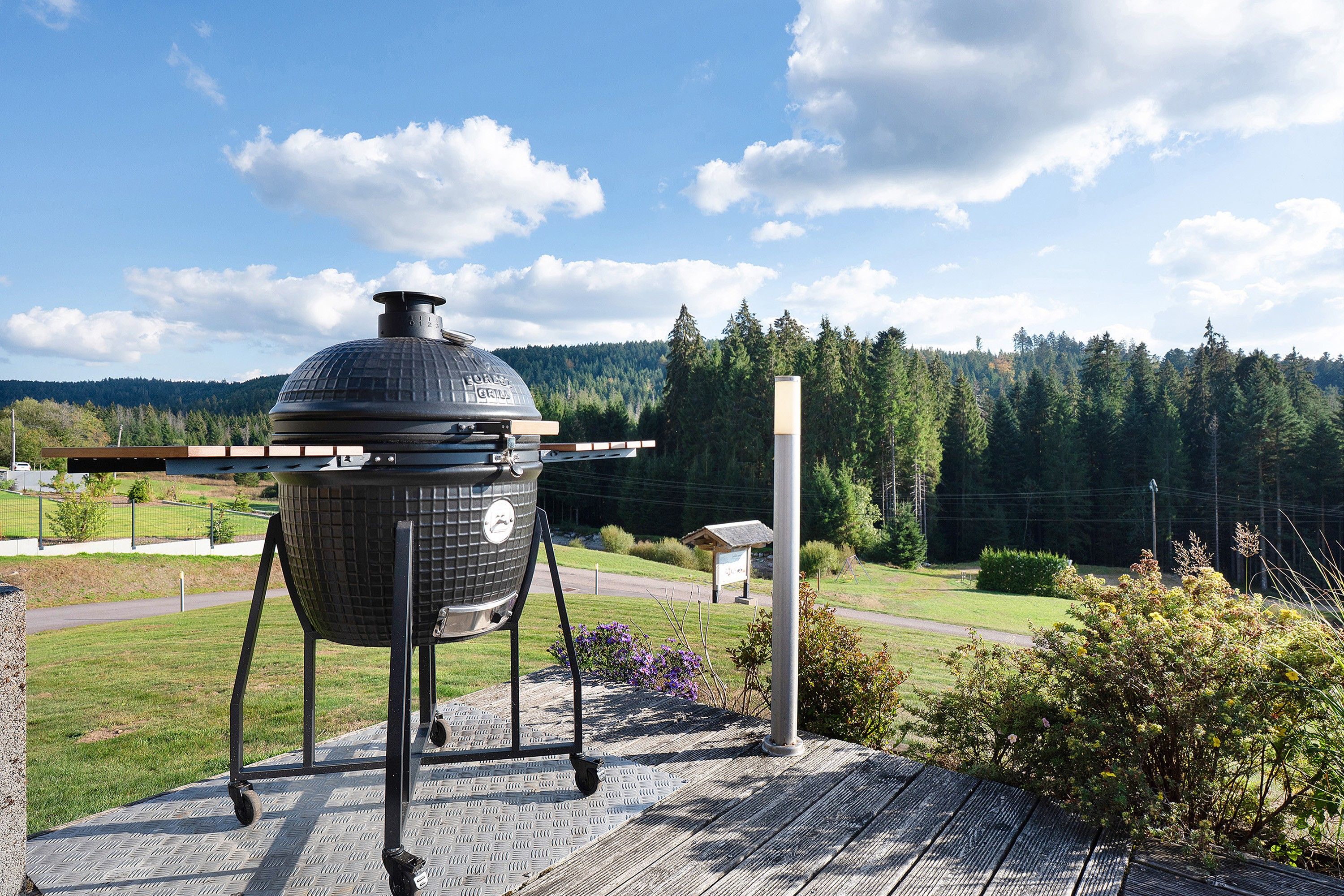 A portable barbecue grill on a patio with a view of a forested hill.