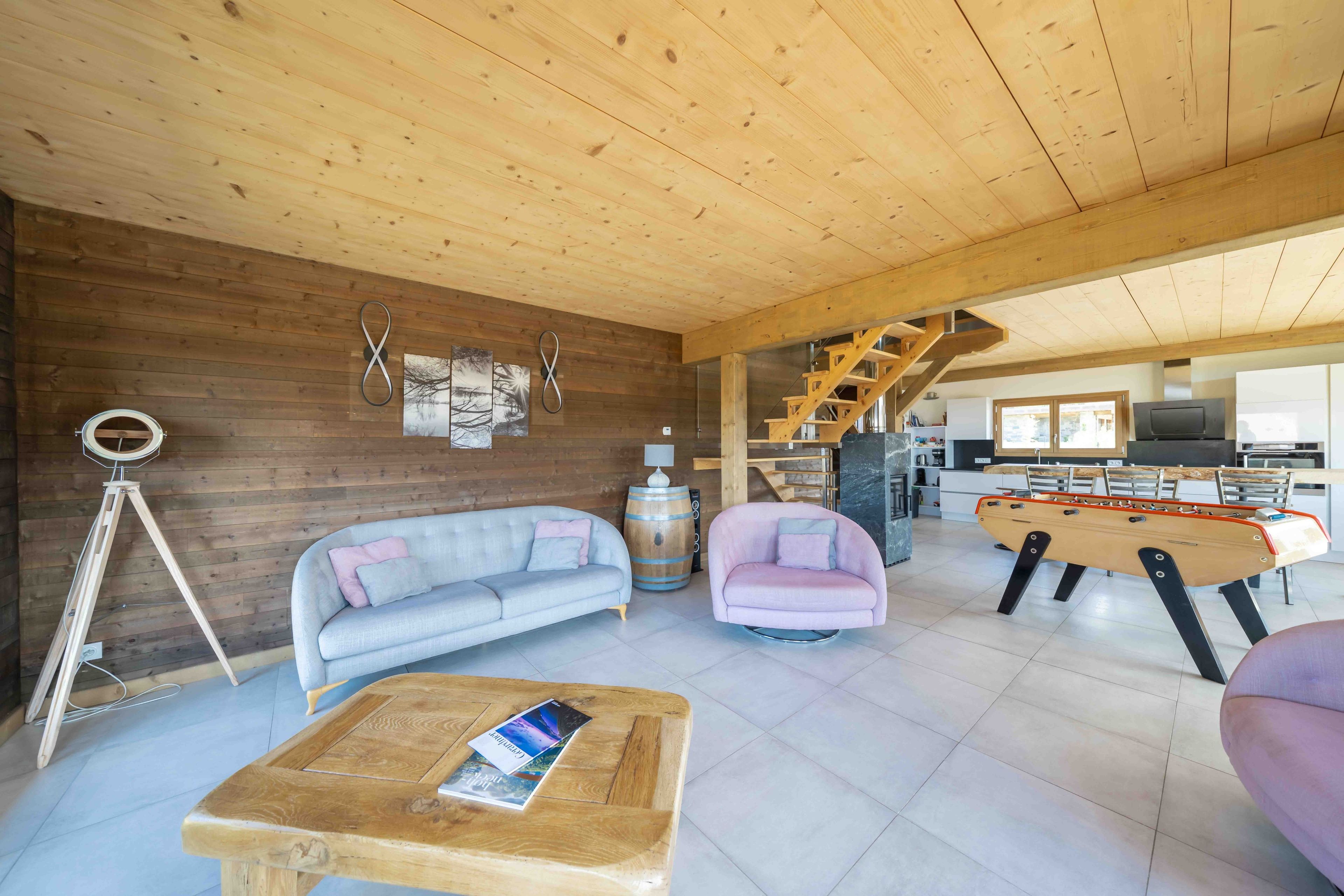 A spacious living area with a wooden ceiling, a sofa, a coffee table, and a foosball table.