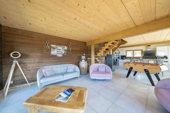 A spacious living area with a wooden ceiling, a sofa, a coffee table, and a foosball table. - Chalet 'L'Alpage' with Mountain View, Sauna and Jacuzzi (Gérardmer)