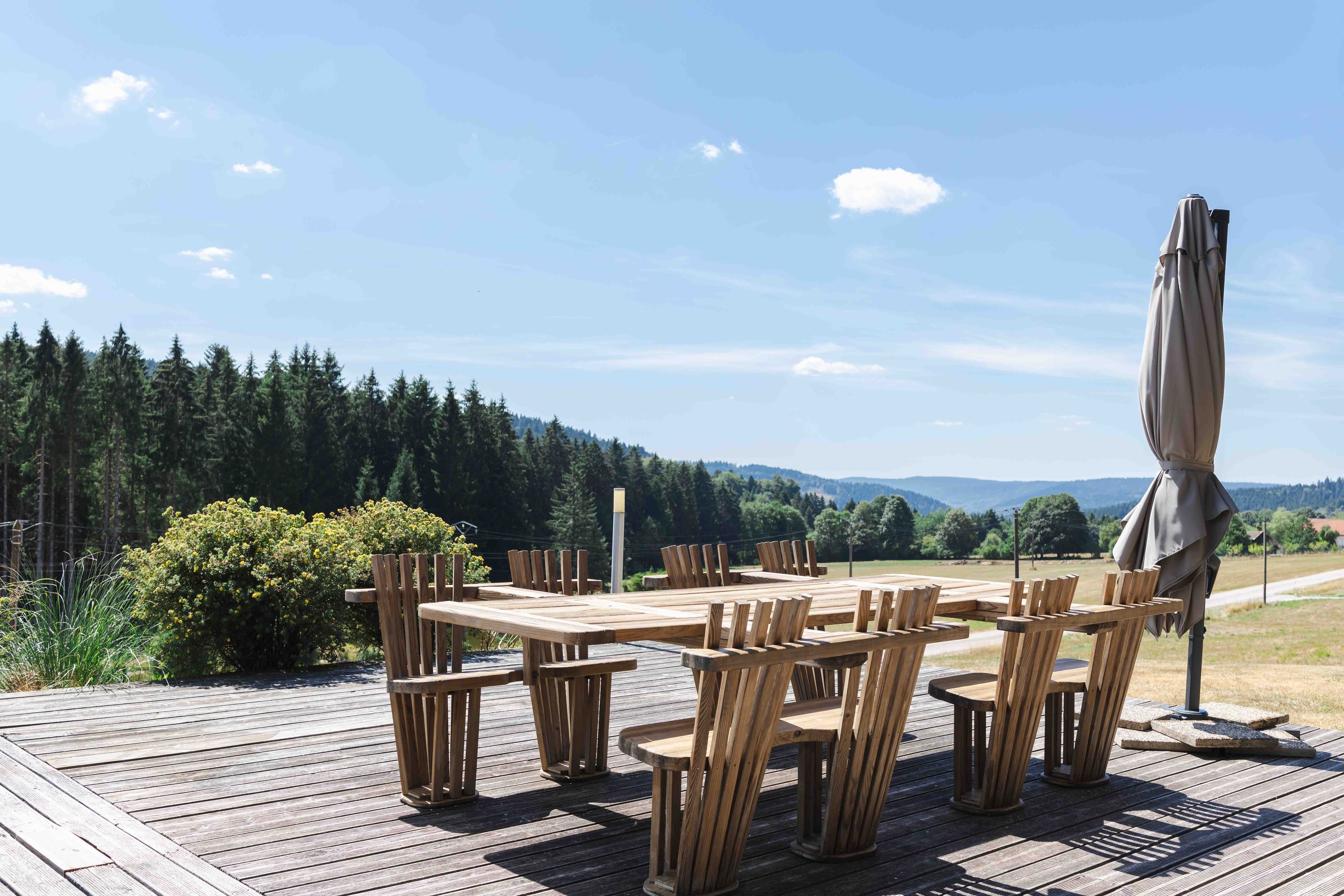 An outdoor wooden deck with a table and chairs, surrounded by a forested landscape.